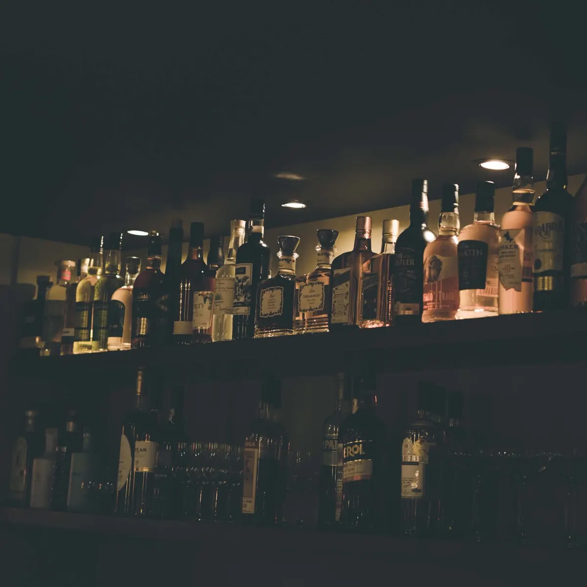 Le bar et ses étagères de spiritueux, éclairés en lumière douce.