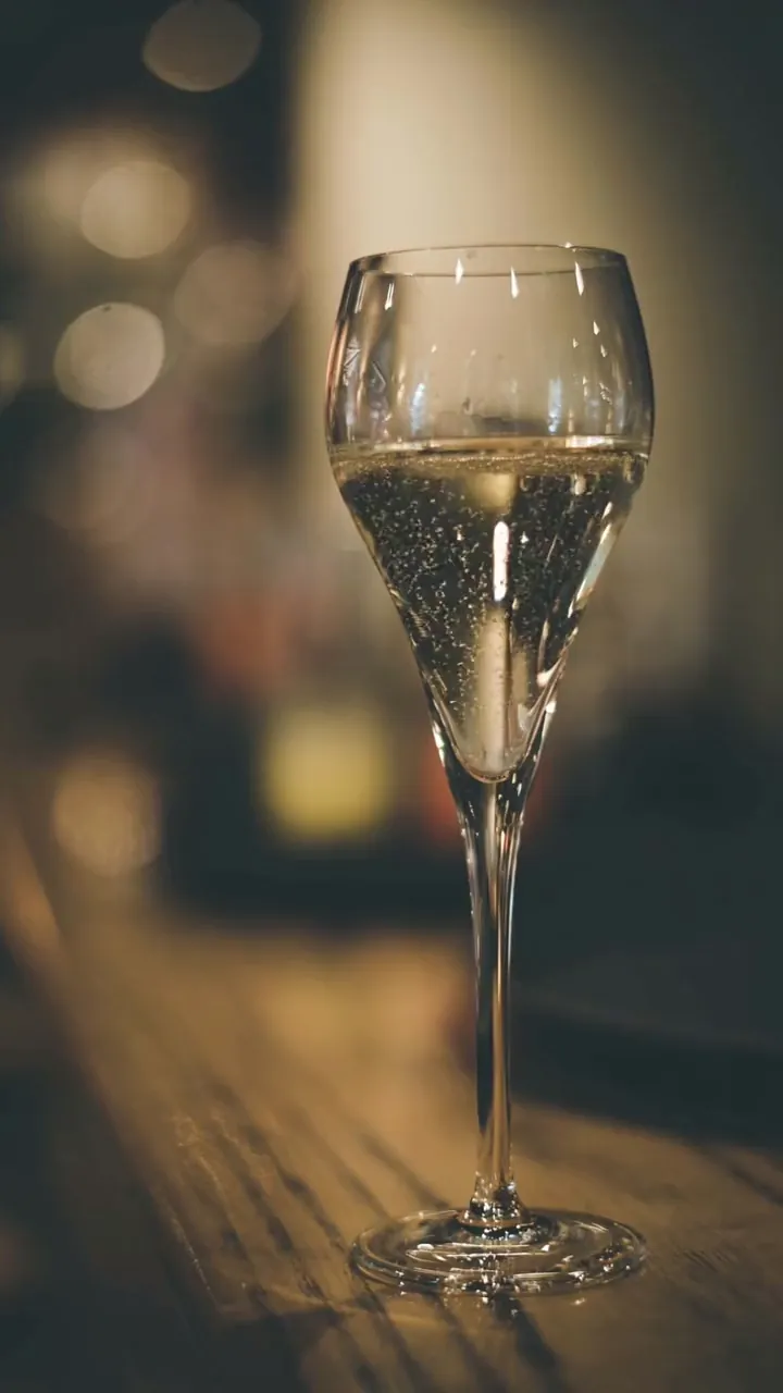Een fluitglas met bubbels op de houten toog van La Ruche, met de verlichting van de bar op de achtergrond.